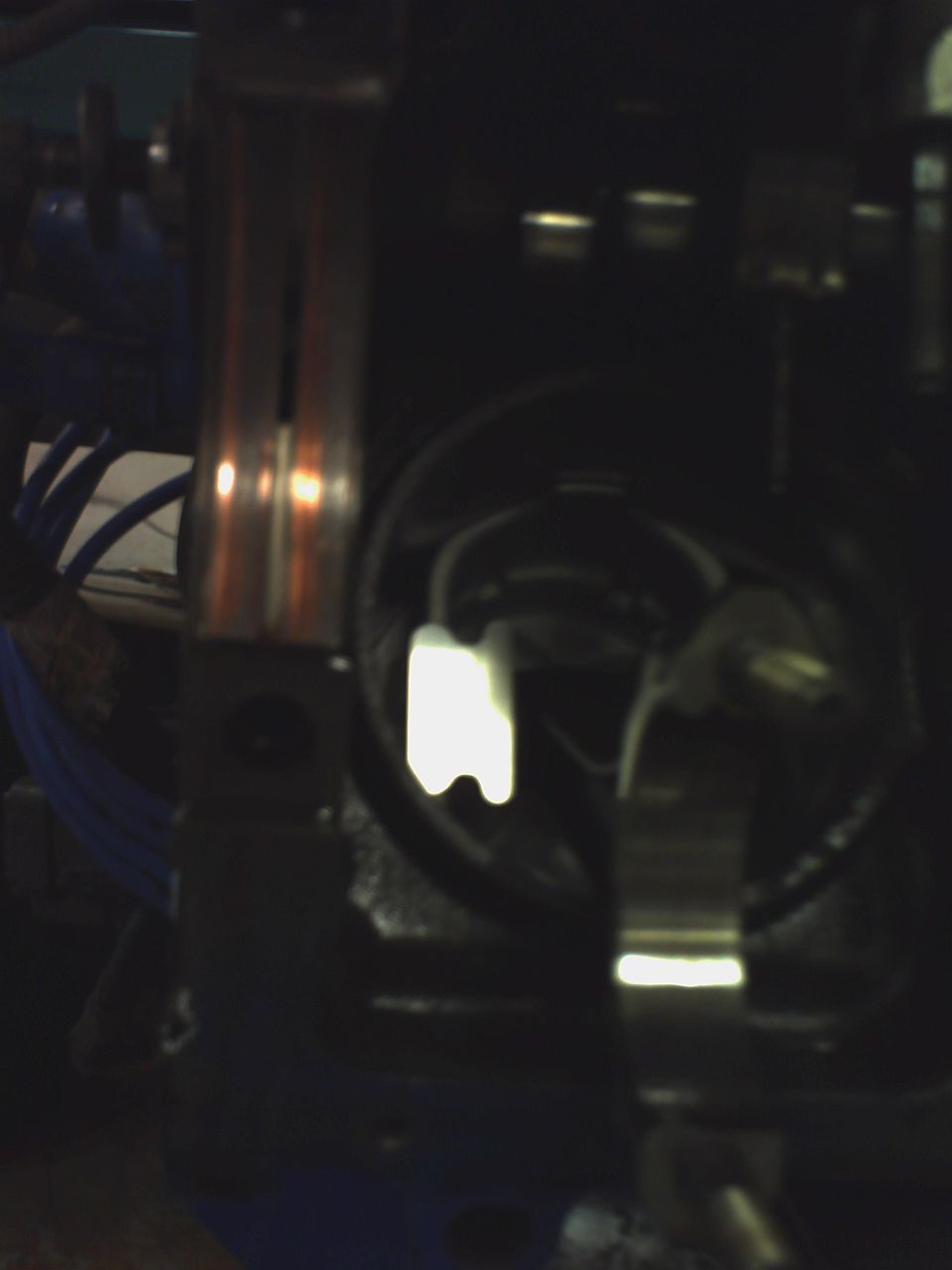 Dark close-up of metal machine part with reflective steel bar and blue wiring