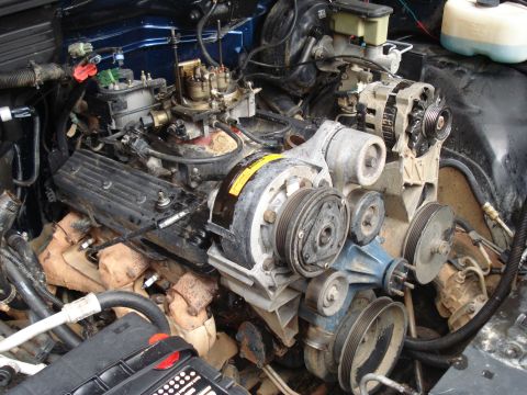 1984 Jeep J-10 - Close-up view of a V8 engine bay, likely from a classic American pickup truck, showing the carburetor, alternator, water pump, and exhaust…