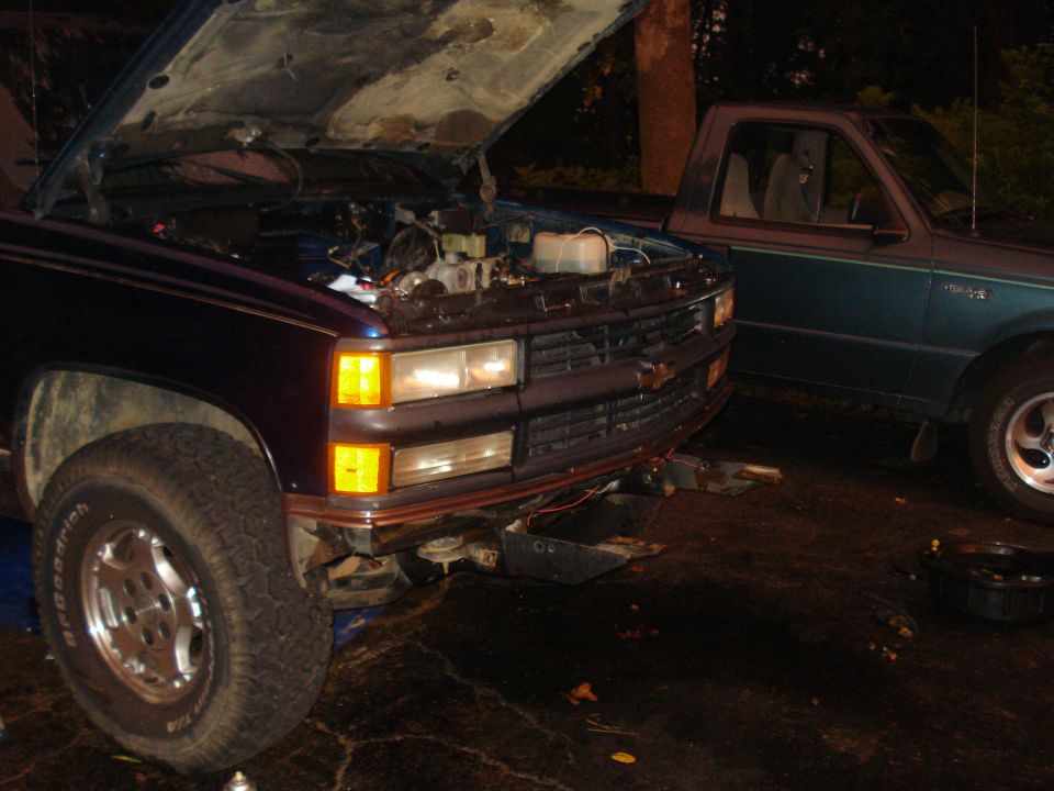 Dark blue pickup truck with hood open, parked next to a teal pickup truck.