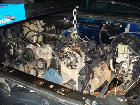 1984 Jeep J-10 - A blue pickup truck engine bay is shown with the engine partially lifted by a chain hoist. Various engine components, hoses, and wiring are…