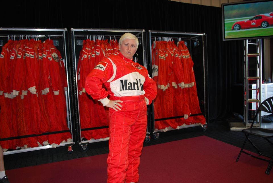 Person in Marlboro racing suit with racks of suits and a TV showing a sports car.
