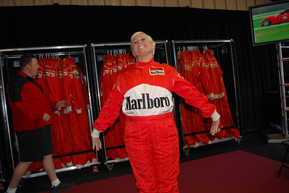 Woman in Marlboro racing suit posing, man in red jacket nearby.