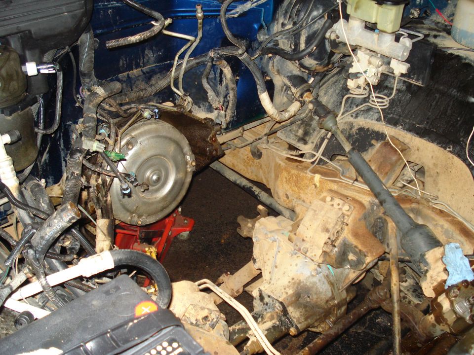 Engine bay of a vehicle showing transmission, torque converter, hoses, and brake master cylinder.