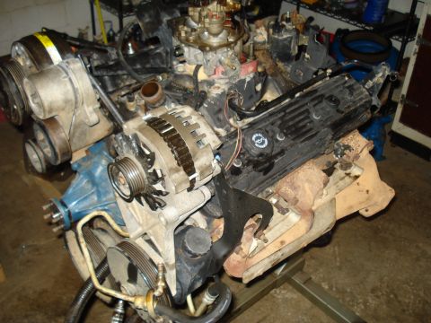 1984 Jeep J-10 - A disassembled V8 engine is mounted on an engine stand in a garage setting. Various engine components, including the alternator, intake man…