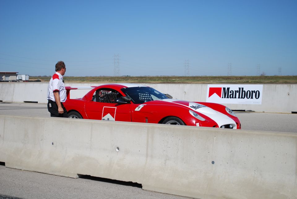 Red race car with white accents on a sandy beach under a clear blue sky