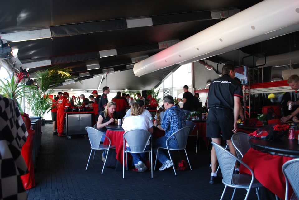 People seated at tables with red tablecloths under a tent with checkered flag decorations