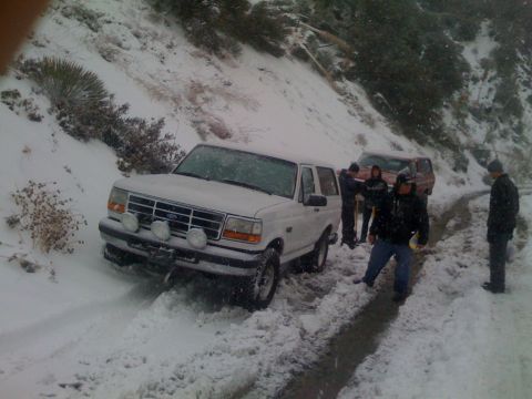 1979 Ford Bronco - A white 1992 Ford Bronco is stuck in the snow on a mountain road, with several people nearby and another vehicle behind it.