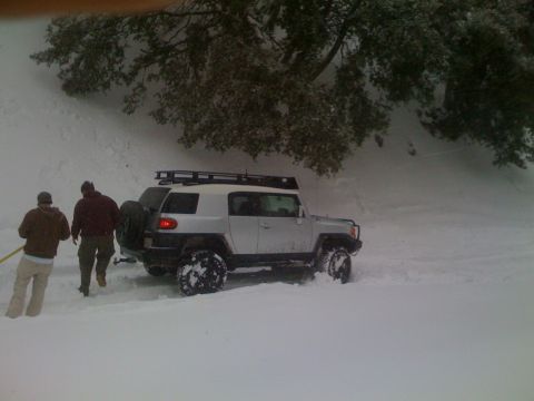 1979 Ford Bronco - FJ Cruiser with roof rack stuck in deep snow, two people are standing next to it.