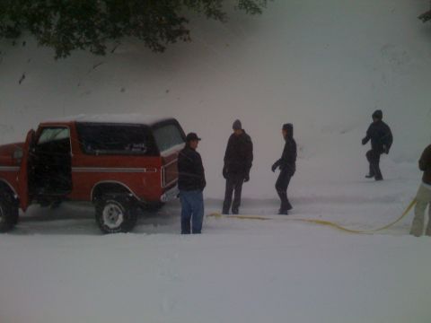 1979 Ford Bronco - A group of people are gathered around a red SUV that appears to be stuck in deep snow.