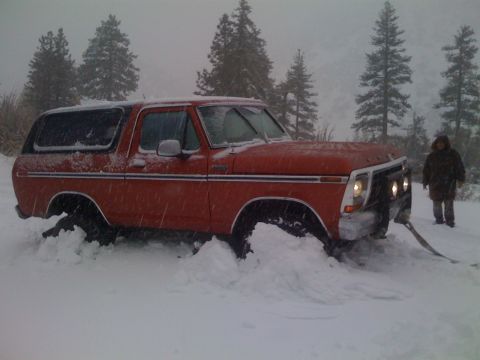 1979 Ford Bronco - A red SUV is stuck in a snowy landscape, with a person observing from behind.