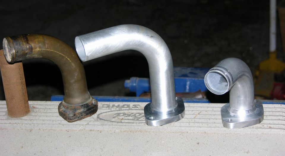 Rusty steel elbow beside two polished aluminum flanged water necks