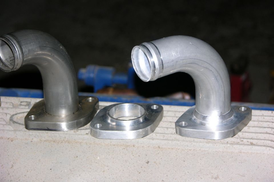 Pair of welded aluminum 90-degree elbow tubes on two-bolt flanges beside a bare flange