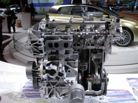 1997 Ford Taurus - Engine cutaway display at an auto show, with a car visible in the background.