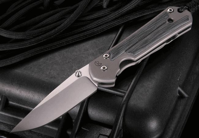 Folding knife with gray handle and silver blade resting on a black case with black cord in background