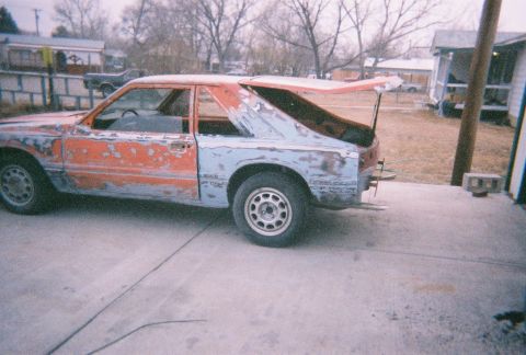 1983 Mercury Capri - This 1983 Mercury Capri is in a state of disrepair, with primer showing through the peeling paint and the trunk ajar.