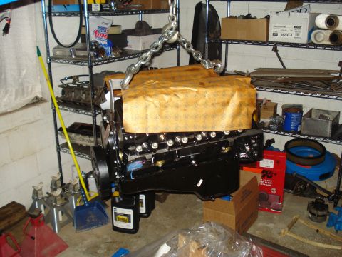 1984 Jeep J-10 - A black engine is being lowered by chains in a cluttered garage environment.