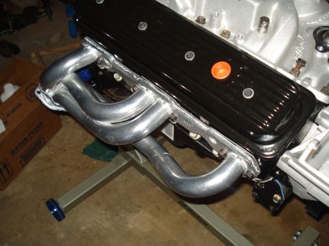 1984 Jeep J-10 - Close-up of engine components, including exhaust headers and valve cover, on a stand.