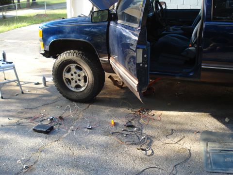 1984 Jeep J-10 - A blue pickup truck is undergoing maintenance with its hood and driver's door open, and various wires are spread across the ground.