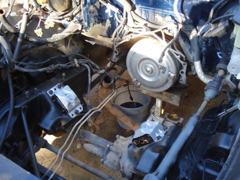 1984 Jeep J-10 - The engine bay is exposed, with the transmission assembly removed and supported by blocks and a jack.