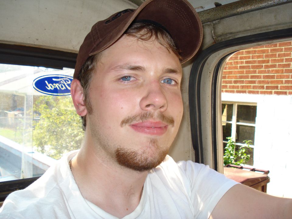 Man wearing a brown baseball cap inside a vehicle, with a Ford logo visible on the window