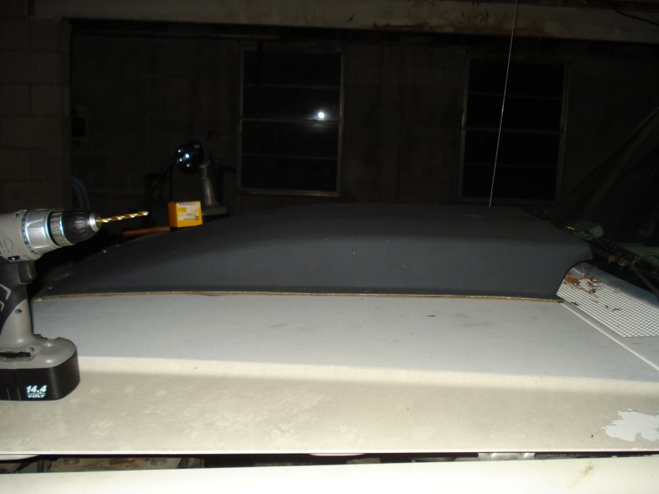 Drill bit poised above a dark-colored vehicle roof section. A yellow box sits behind the drill