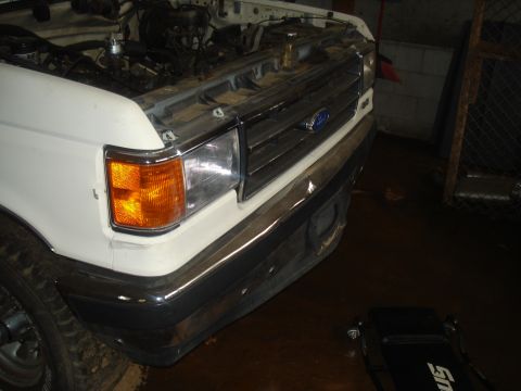 1991 Ford Bronco - The front grille and headlights of a white Ford truck are visible, with the hood open to reveal the engine compartment.