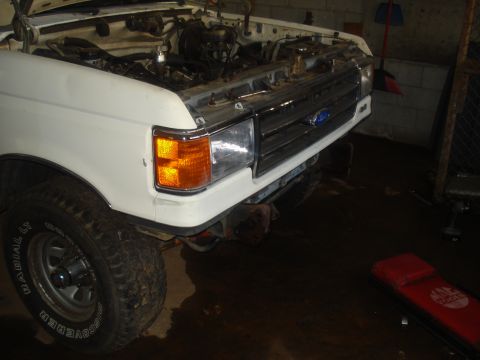 1991 Ford Bronco - Front view of a white Ford truck with its hood open, revealing the engine and a chrome grille. The year appears to be 1987.