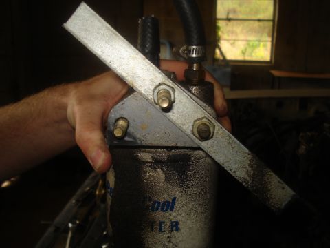 1991 Ford Bronco - A hand holds a specialized tool for removing an oil filter, with a hose connected to the device.