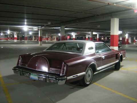 1988 Mercury Grand Marquis - Dark maroon Lincoln Continental Mark V personal luxury coupe with vinyl top and Continental spare-tire hump, parked in a concrete garage.