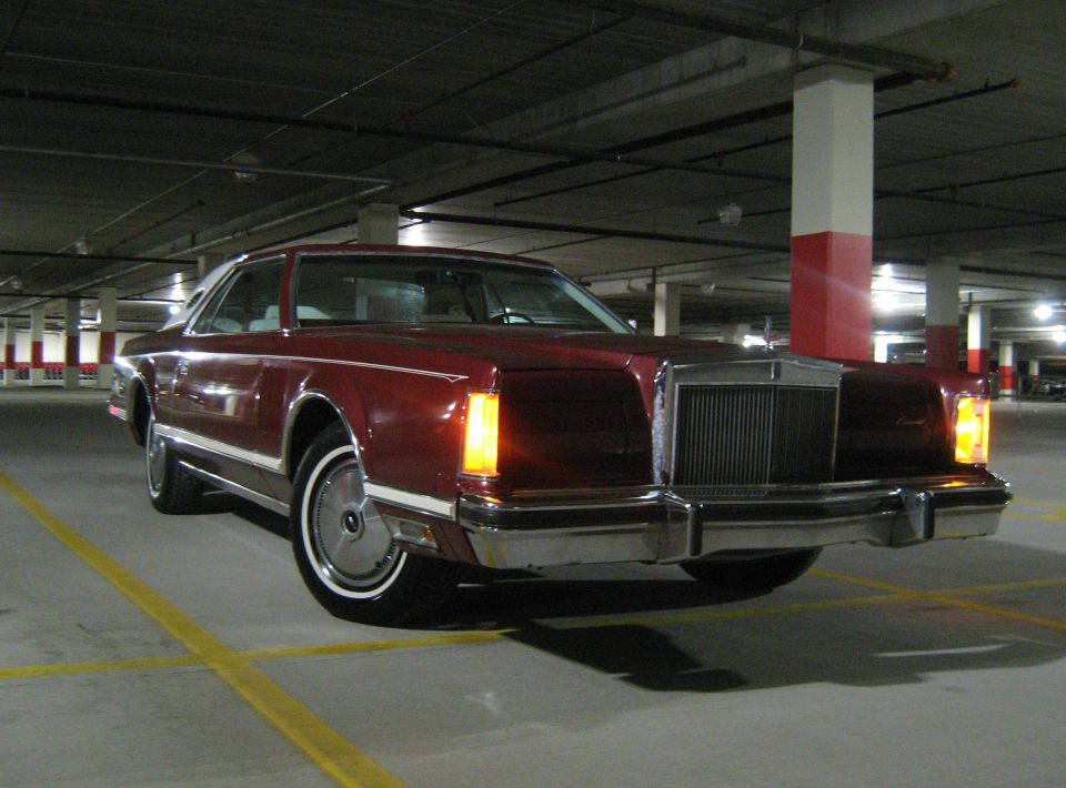 Maroon coupe with white vinyl top parked in a parking garage. Front grille and headlights visible