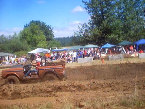 1976 Ford F-100 - A 1976 Ford F-100 Bronco navigates a muddy track during a race event with spectators in the background.