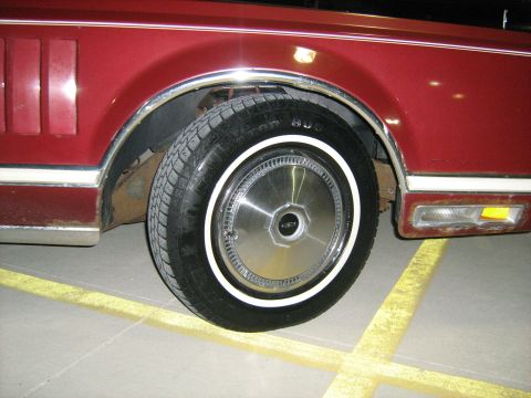 1988 Mercury Grand Marquis - Close-up of a red car's rear wheel and fender, revealing details of its design and condition.