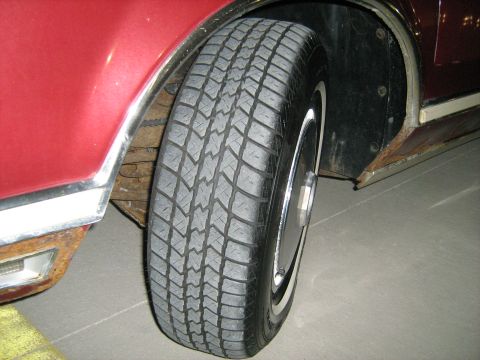 1988 Mercury Grand Marquis - Close-up view of a red car's wheel and fender area, showing chrome trim and a whitewall tire.