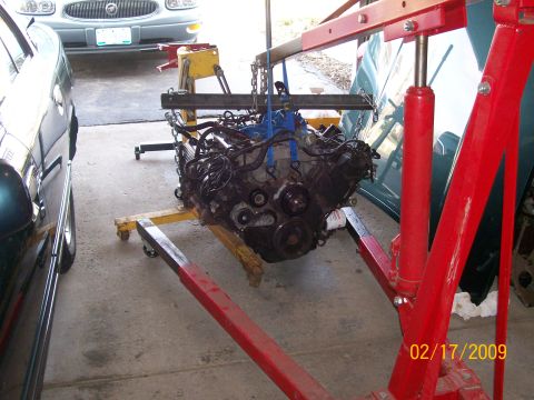 1995 Mercury Grand Marquis - An engine is suspended by a red engine hoist, with other vehicles partially visible in the garage.