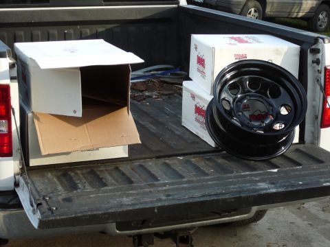 1991 Ford Bronco - Boxes and a wheel are loaded in the bed of a pickup truck, with another vehicle parked behind.