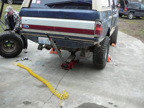 1991 Ford Bronco - A man works on a lifted Ford Bronco with a custom rear bumper and off-road tires.