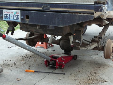 1991 Ford Bronco - The rear suspension of a truck is shown with a floor jack supporting the axle during maintenance.