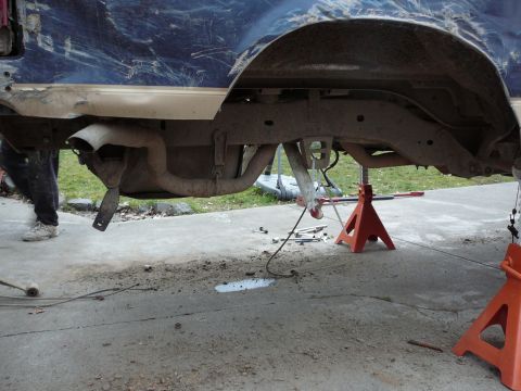 1991 Ford Bronco - The rear axle and exhaust system of a blue vehicle are visible while it is supported by jack stands.