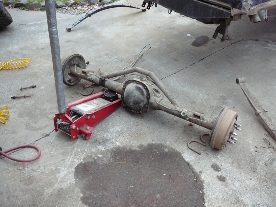 Rear axle assembly with drum brakes on a red hydraulic jack, with a leaf spring nearby