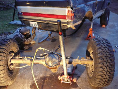 1991 Ford Bronco - A person is working on the rear axle of a Ford truck, which is supported by jack stands.