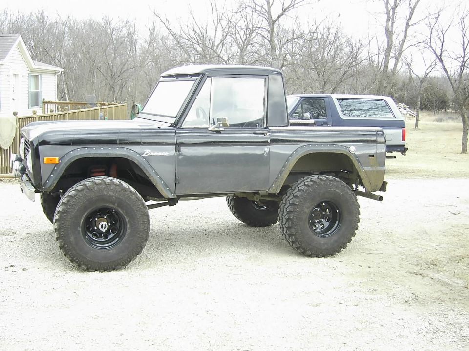 Gray Ford Bronco with black top, lifted suspension, and large off-road tires, viewed from the side
