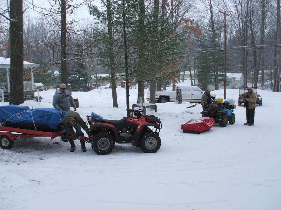 People loading ATVs and sleds in a snowy wooded yard