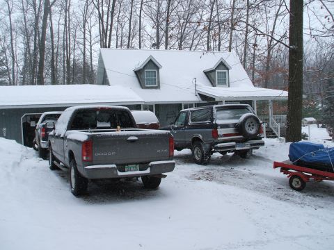 1990 Ford Bronco - A gray and blue Ford Bronco is parked in the snow next to a house, with a Dodge pickup truck in the foreground.