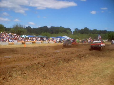 1976 Ford F-100 - Trucks race through mud as spectators watch from the sidelines at a mud drag event.