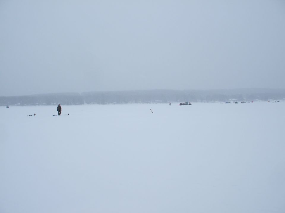 People ice fishing on a frozen body of water with a treeline in the background