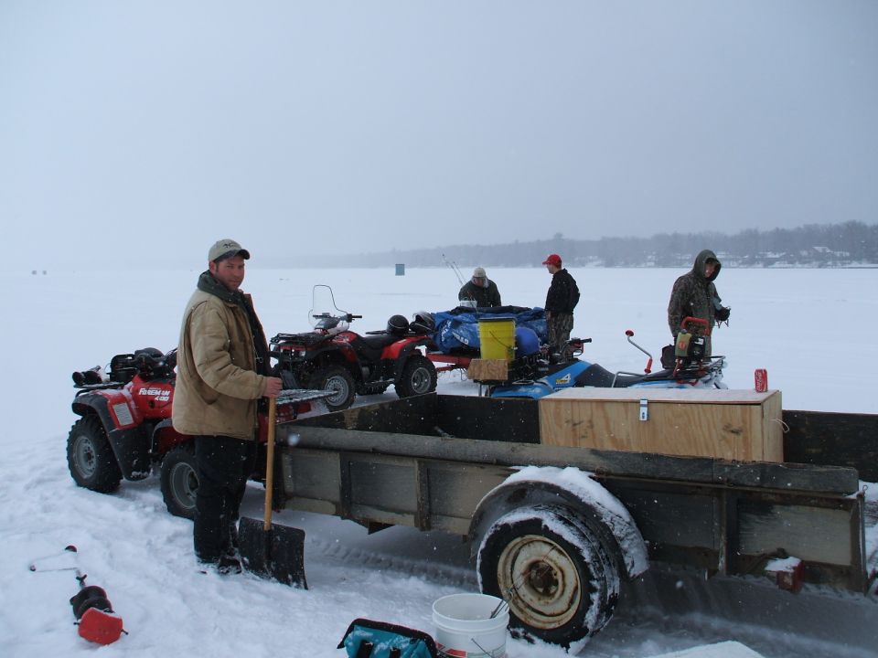 Trailer loaded with gear and four-wheelers on a frozen lake with people