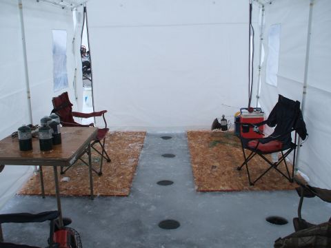1990 Ford Bronco - Interior of an ice fishing tent set up with chairs and fishing gear, showing holes cut into the ice floor.