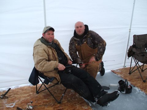 1990 Ford Bronco - Two men are ice fishing inside a tent, with fishing rods and gear visible on the ice and wooden floor.