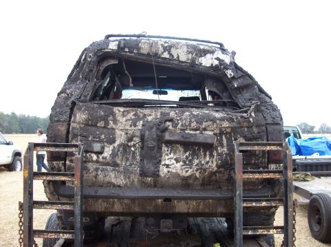 1986 Ford Bronco - This heavily mud-covered vehicle is being transported on a trailer, with another vehicle and tarp in the background.