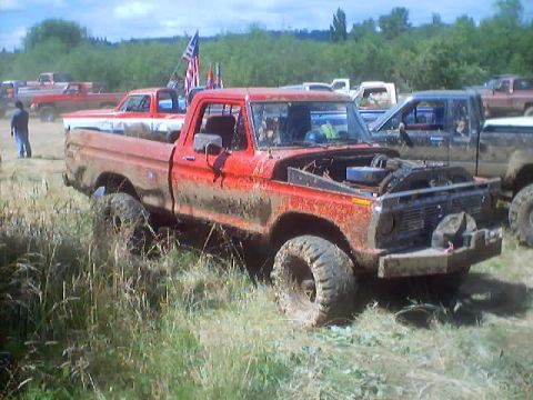 1976 Ford F-100 - Several trucks are gathered at a muddy event, with one red Ford pickup prominently displayed.
